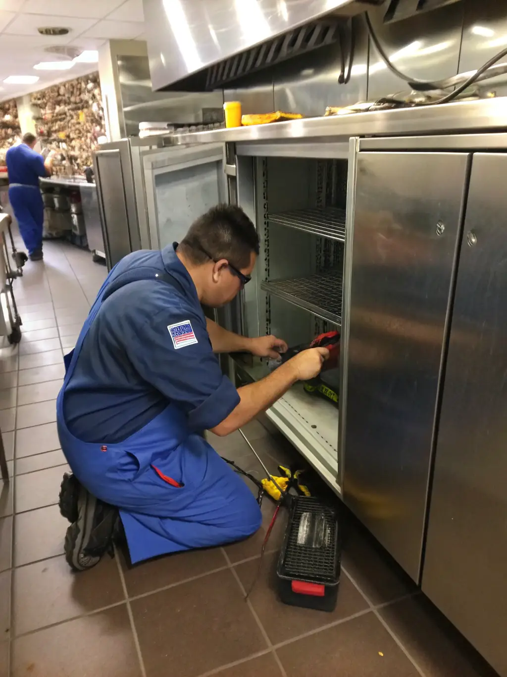 A Frostline technician meticulously repairing the ice maker component of a commercial refrigerator in a restaurant setting.